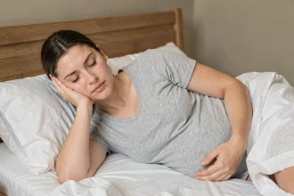 Femme enceinte du premier trimestre allongée sur le côté dans son lit, exprimant la fatigue naturelle du début de grossesse